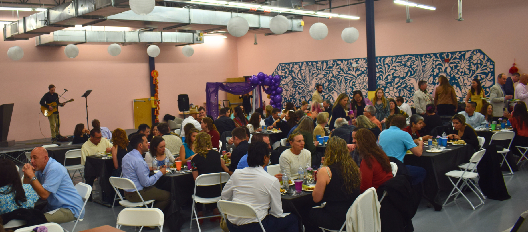 A lively event with people dining and a musician performing on stage.