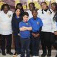 Group of people smiling together, wearing matching blue shirts and white tops.