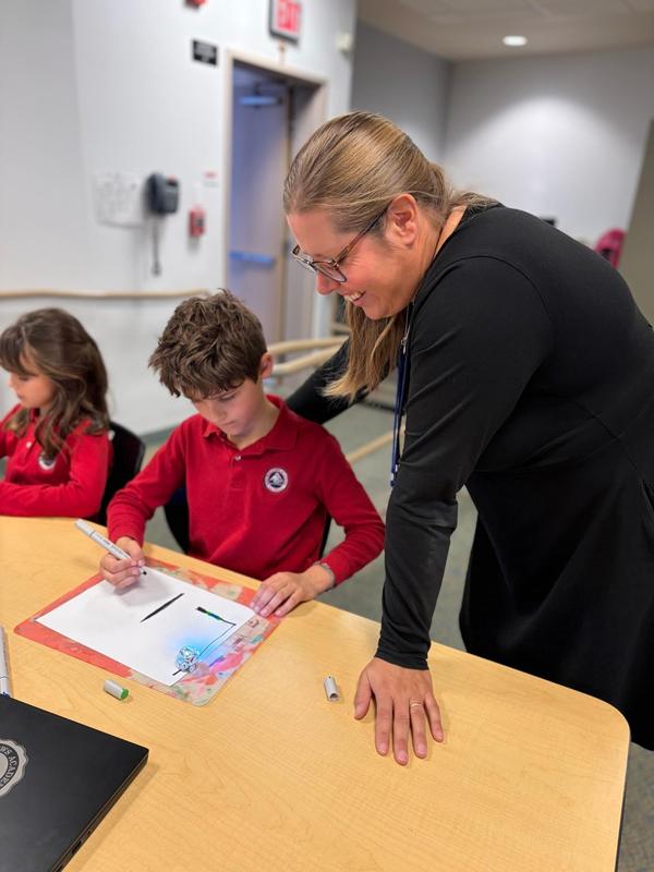 teacher sits next to 2nd grade student to watch his ozobot move
