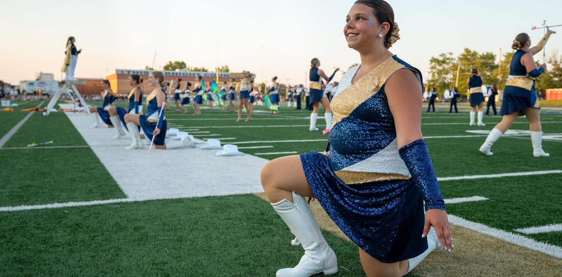 A marching band member kneeling on the field, wearing a sparkling outfit.