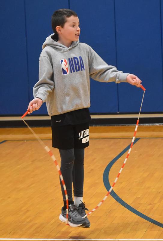 A boy jumps rope in a gym, wearing a gray NBA sweatshirt and black shorts.