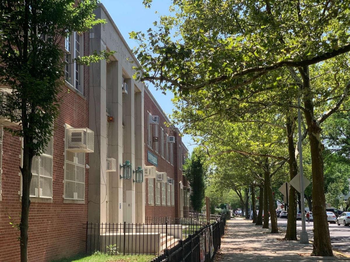 Brick school building beside a tree-lined sidewalk on a sunny day.