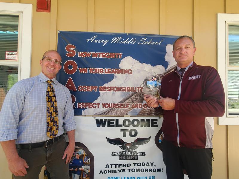 two men posing with an award in front of a school banner