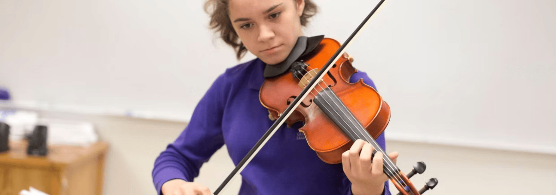 Student playing violin during practice in a classroom setting.