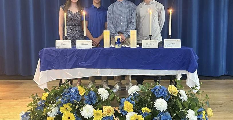Students at a ceremony with candles and flowers on a table.
