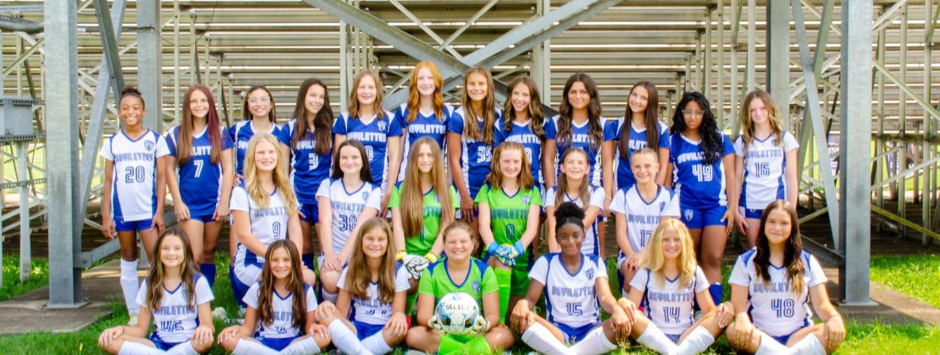 A large group of young female soccer players posing together on a field.