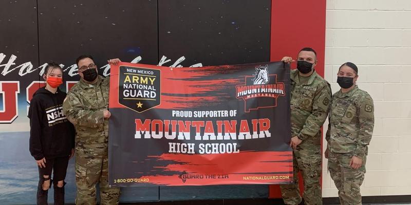 Four people, including Army personnel and a student, hold a banner for Mountainair High School.