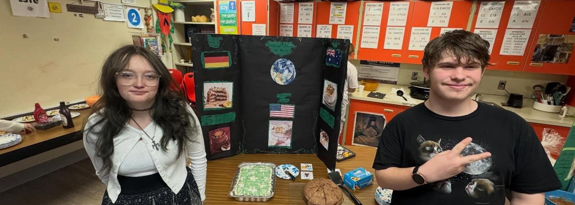 Two students presenting a project display with various items and flags in a classroom.