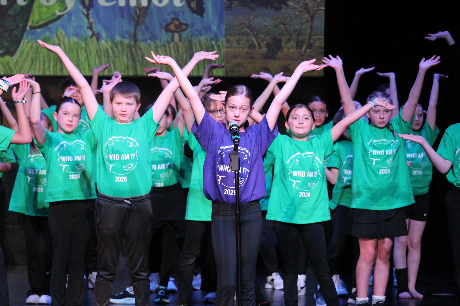 boys and girls in purple and green shirts dance on stage