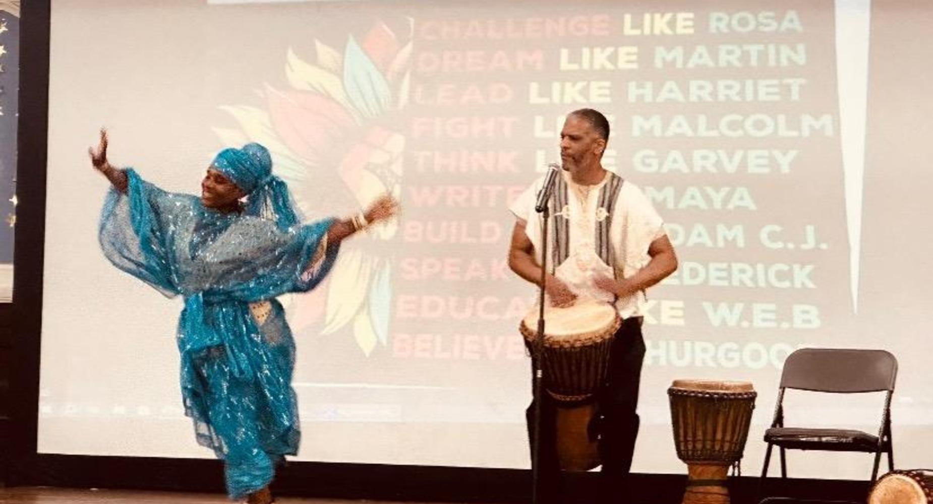 Female African dancer in blue sparkly outfit and a male drummer with a drum attached around his waist