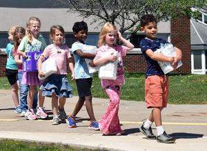 A group of children walking together, each carrying bags of diapers.