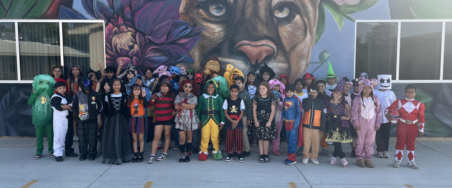 A large group of children in various costumes posing in front of a mural.
