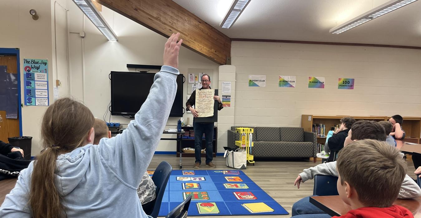 Students watch a presenter at the front of the library, who is holding a piece of parchment.