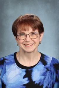 Woman with short hair and glasses in a blue patterned top, smiling at the camera.