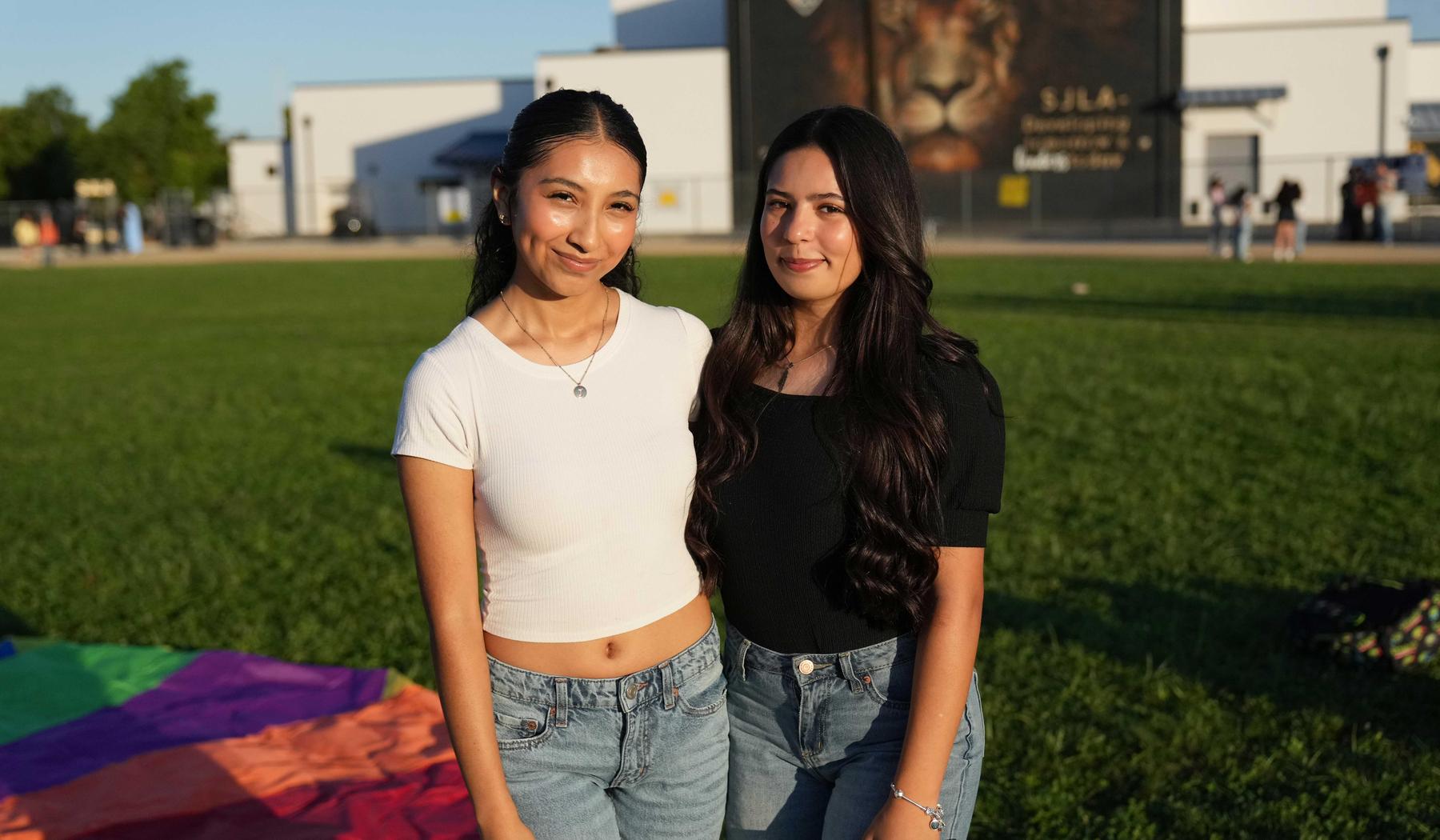 Two girls standing on SJLA field with school mural in background
