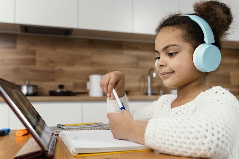 Girl stis at a desk with headphones while she works on a computer.