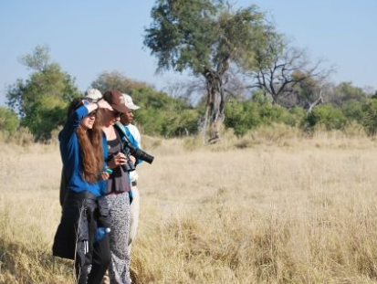 Students hold binoculars on a grassland area with trees in the background