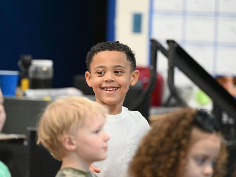 A smiling boy stands with a group of children in a classroom.