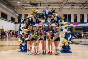 girls in uniforms standing in a gym with a balloon arch