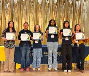 Two teachers and four students holding certificates and standing in front of a gold curtain