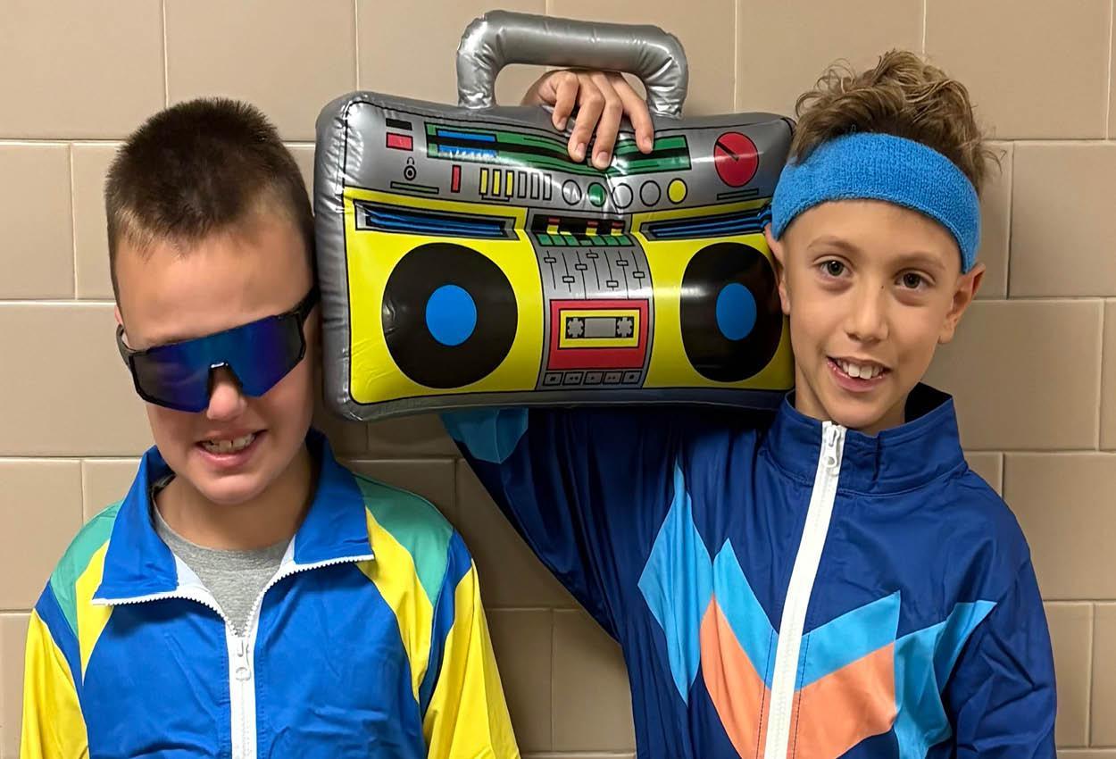 Two boys posing with a toy boombox, wearing colorful sports outfits and sunglasses.