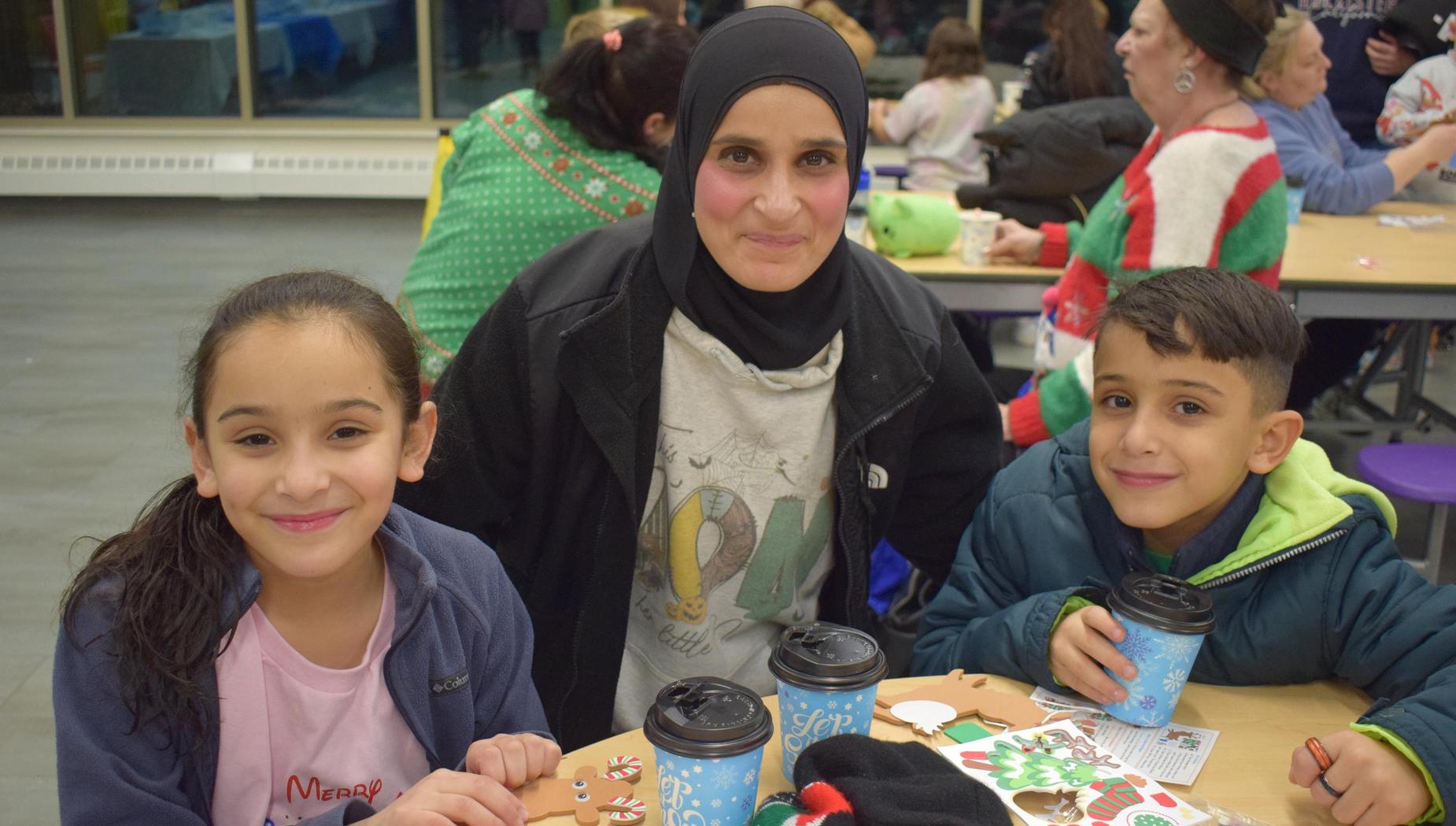 A woman and two children sit at a table with crafts and drinks, all smiling and enjoying the event.