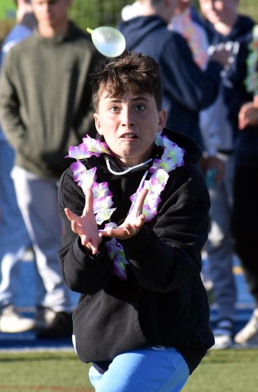 A boy in a lei attempts to catch a small ball mid-air.