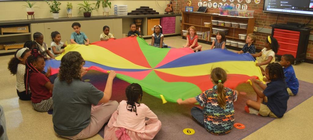 students sit in circle playing with parachute