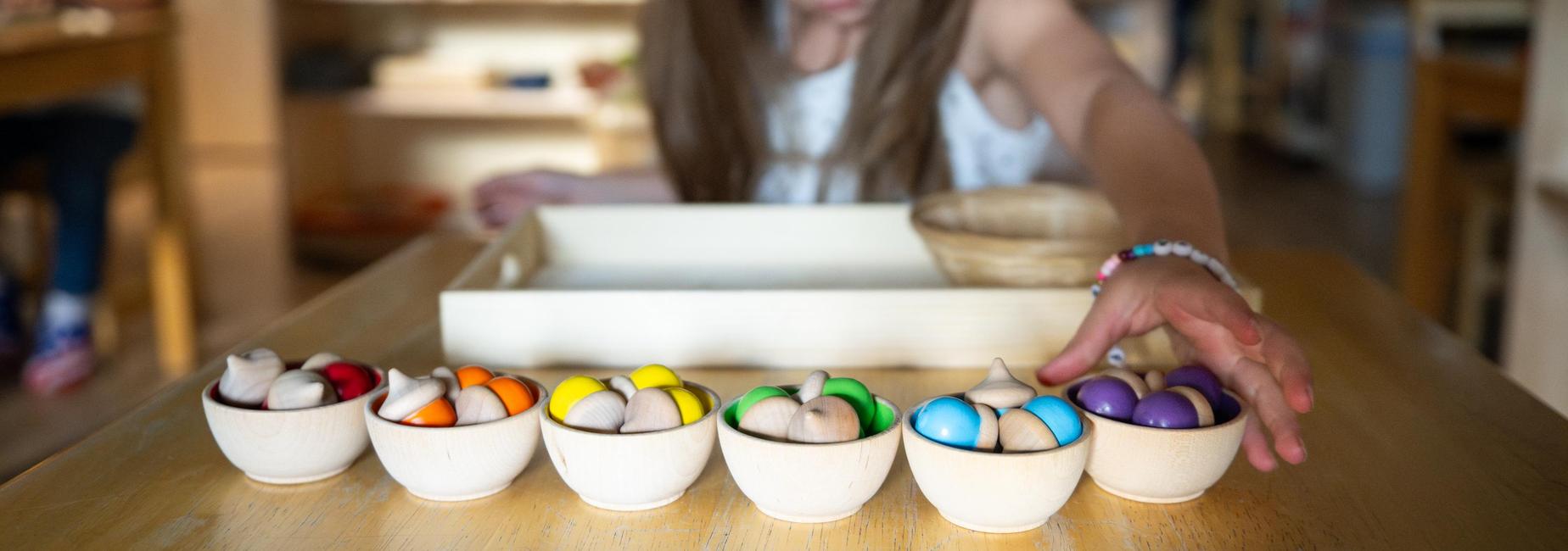A girl arranging colorful wooden beads in bowls on a table.