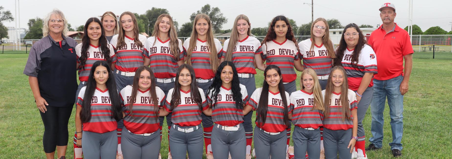 Group of female softball players in red and gray uniforms posing with coaches outdoors.