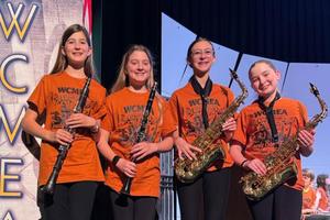 4 Penn Middle students are pictured holding their instruments and standing on the stage