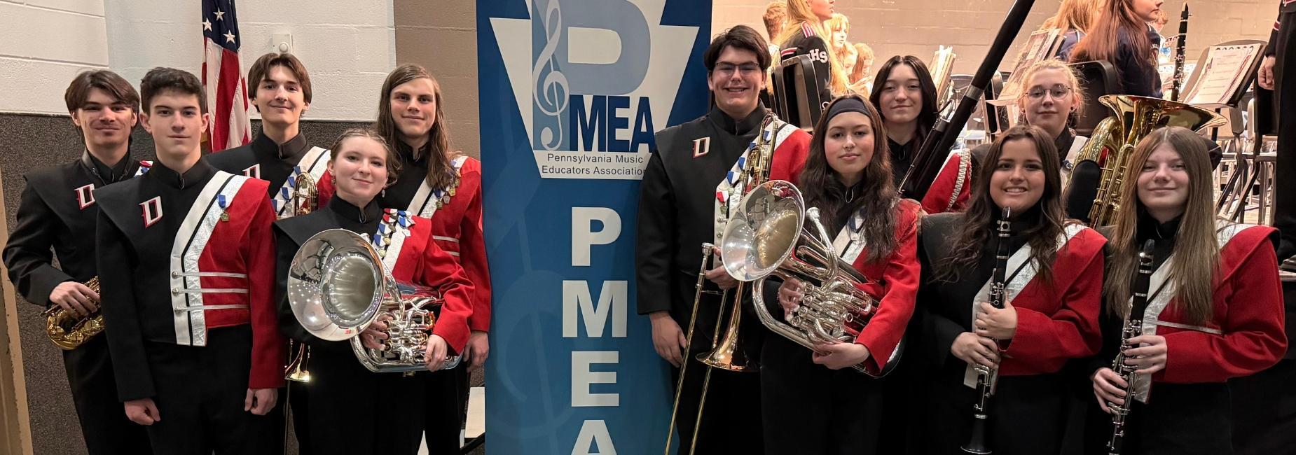Band members in uniforms posing with a PMEA banner.