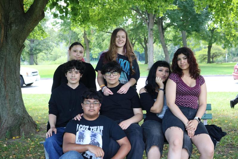 A group of students sit on a bench outside.