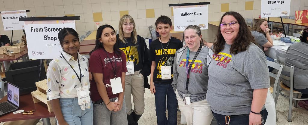Group of students and adults posing at an event with signs in the background.