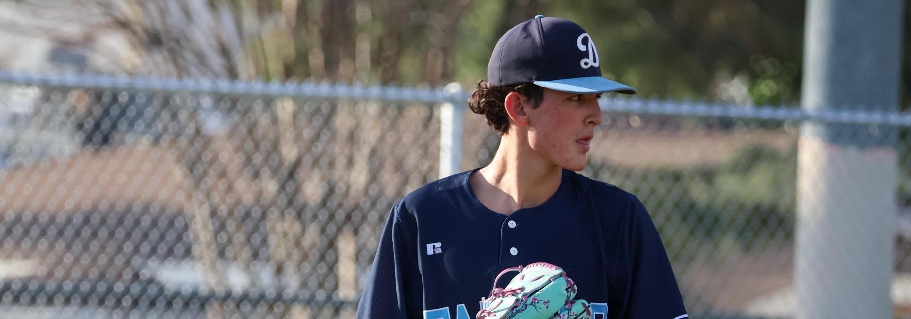 A young baseball player stands ready on the field, wearing a team jersey and glove.