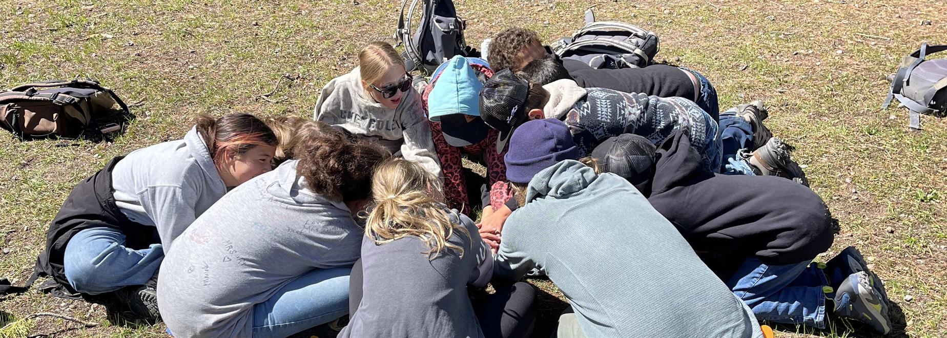 Children huddled together on the ground, engaged in an activity in a grassy area.