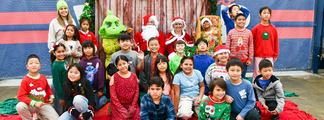 Children dressed in Christmas attire pose with characters in front of a festive setting.