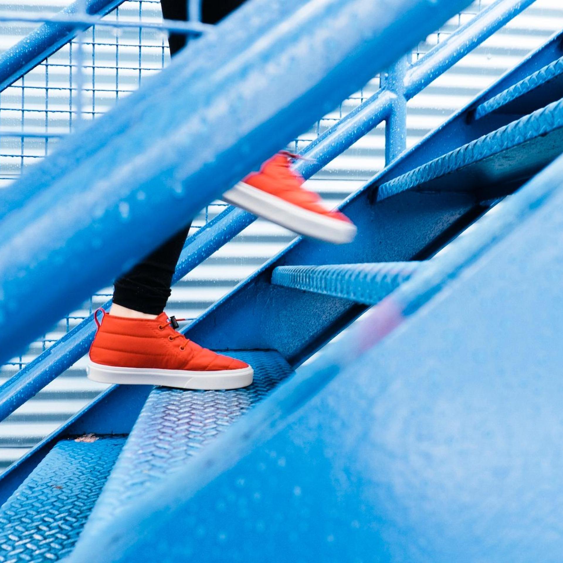 A person wearing red shoes climbing blue metal stairs.