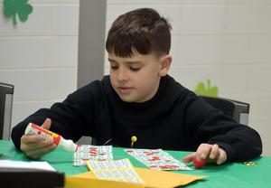 Boy focused on bingo cards with glue and playing pieces.