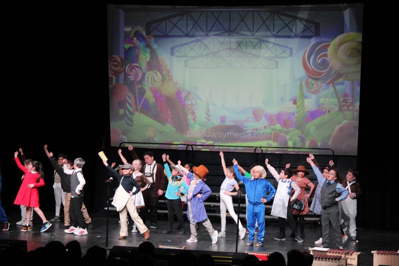 Elementary school students perform an excerpt from Wonka on stage.