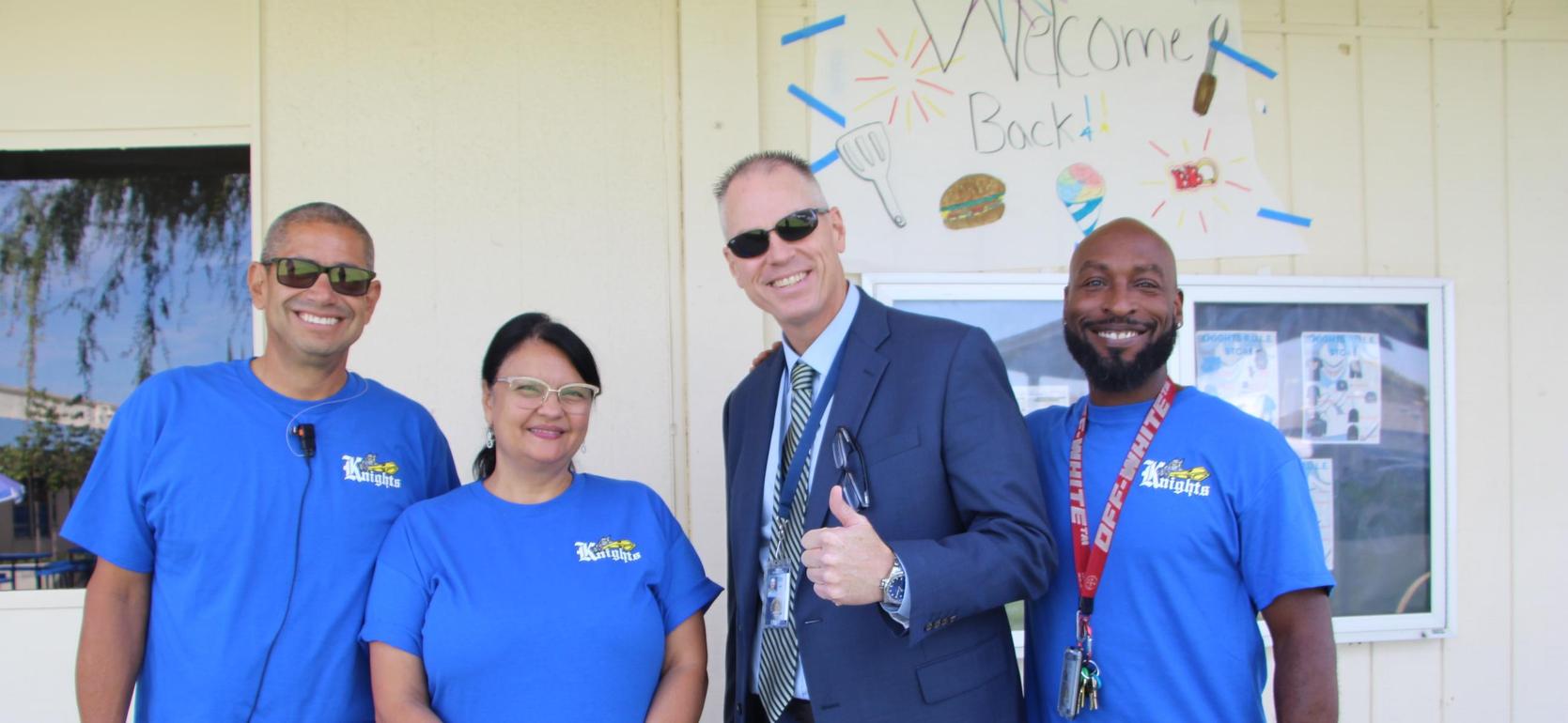 Four people smiling together outside a building, all wearing blue shirts.