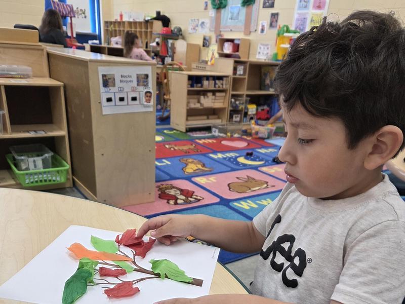 Child creating a paper collage with colorful leaves and branches on a table.