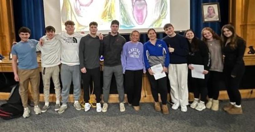 Students gathered in an auditorium with a large artistic backdrop and a teacher.