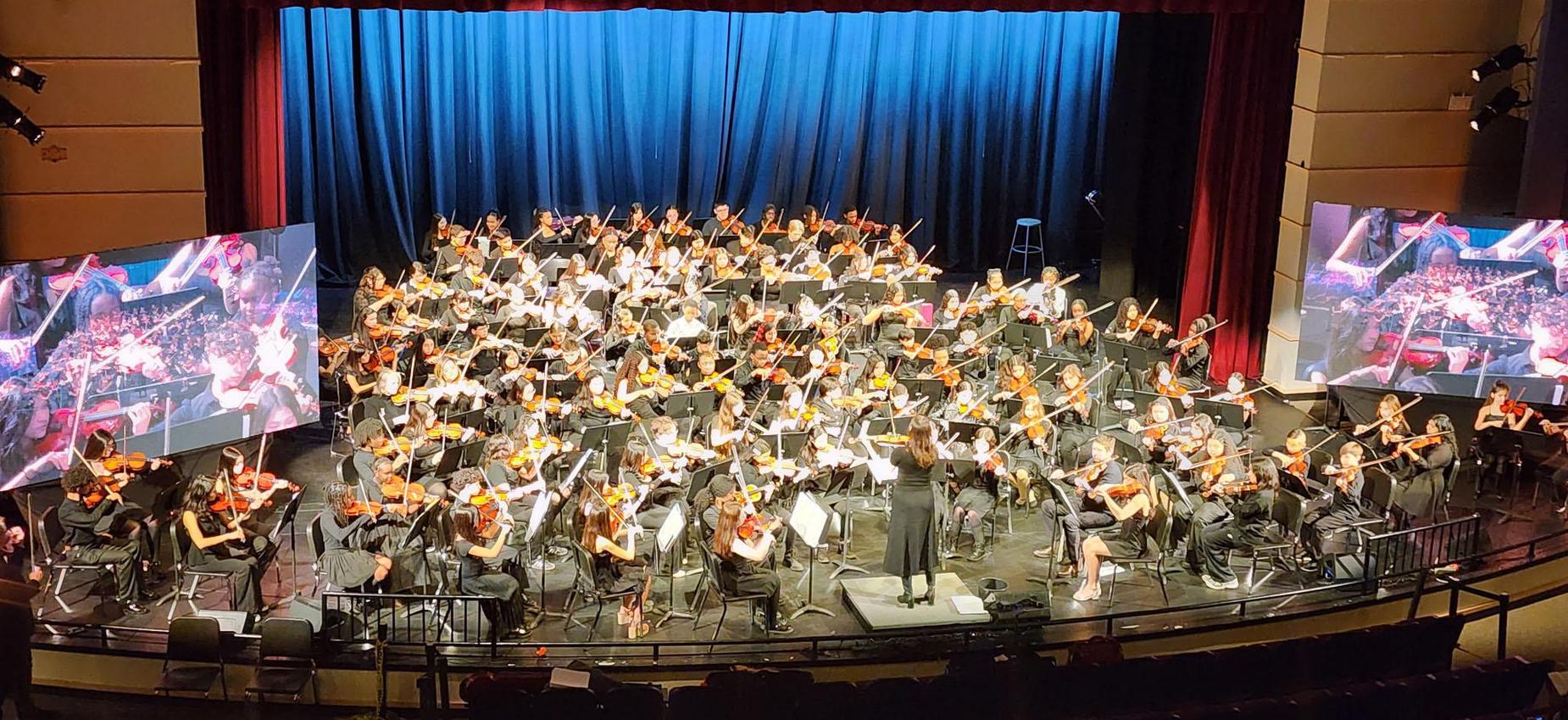 A large orchestra performing on stage with a conductor.