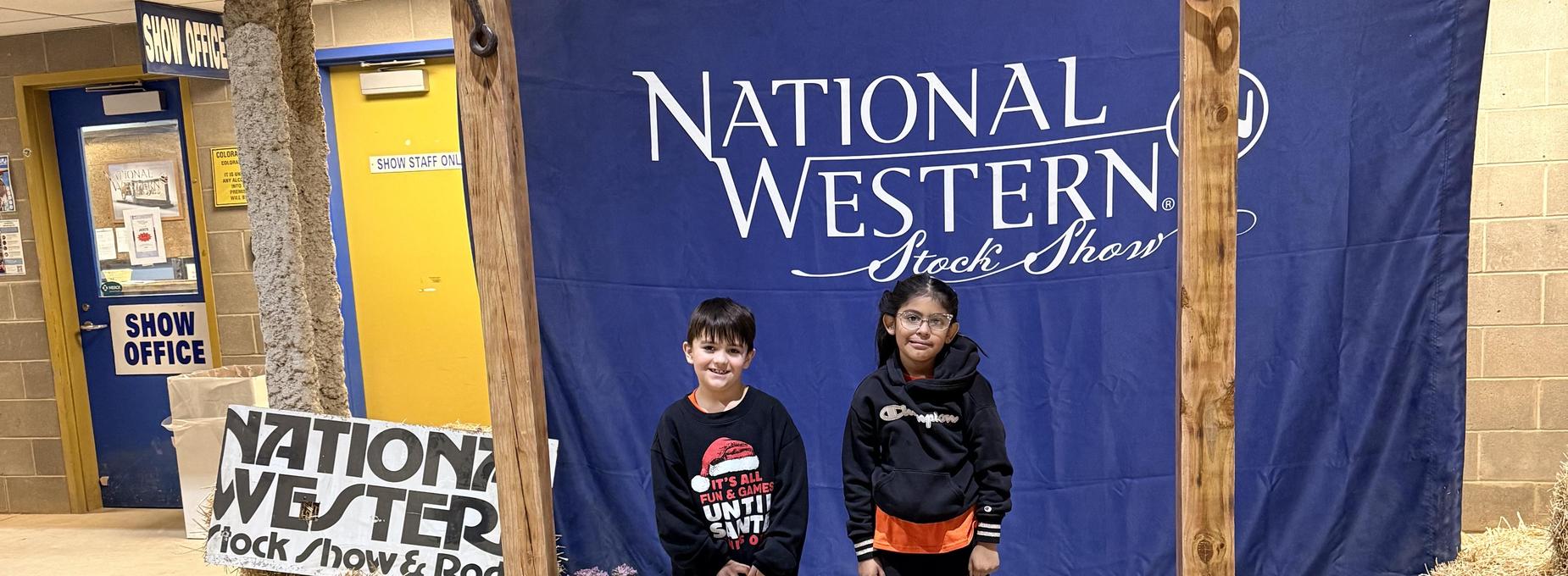 Two children smiling in front of a National Western Stock Show backdrop
