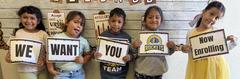 Group of children holding signs, promoting enrollment for a program.