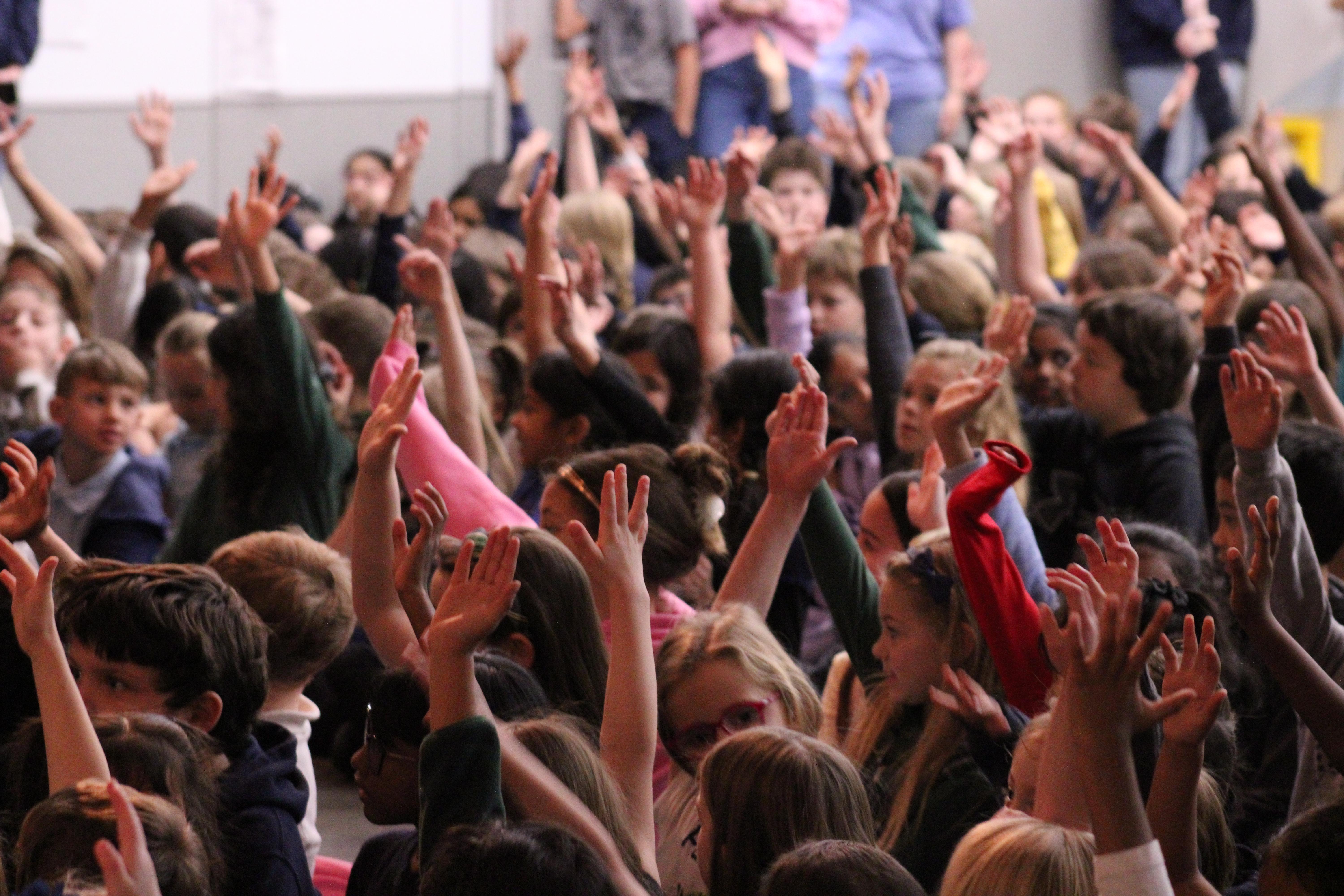 Students raise their hands during assembly