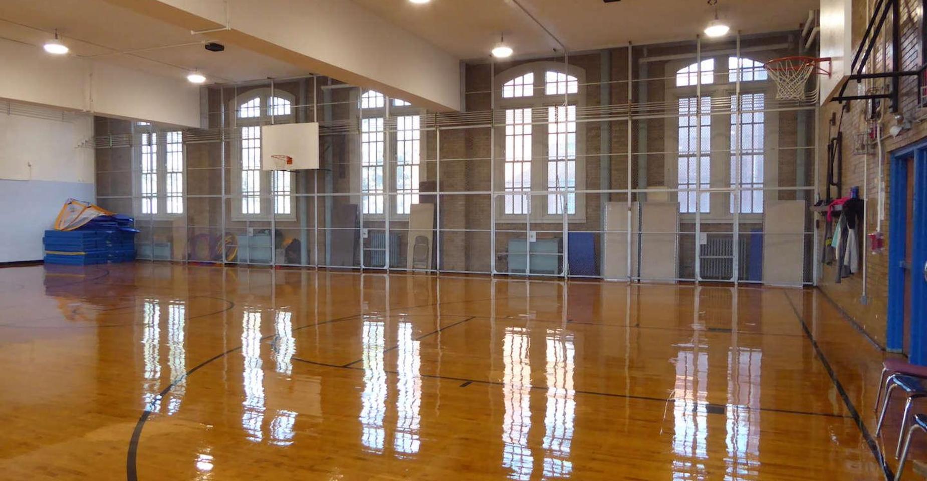 Indoor gymnasium with shiny wooden floors and large windows.