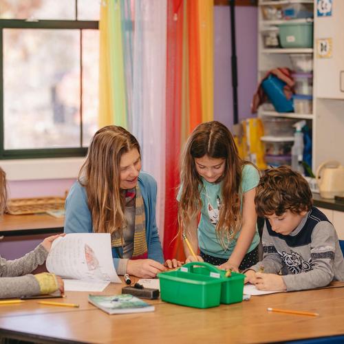 A teacher assisting two children with activities at a classroom table.