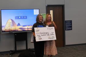 Two women holding a large check for $750 in front of a screen.